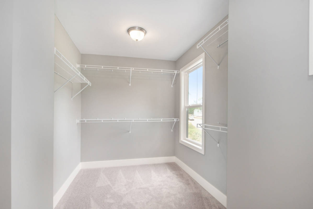 A small, empty walk-in closet with light gray walls, white wire shelving, a ceiling light, and a window.