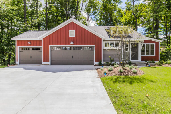 austen1 A red and white suburban home with double garage doors, surrounded by green trees under a clear blue sky.