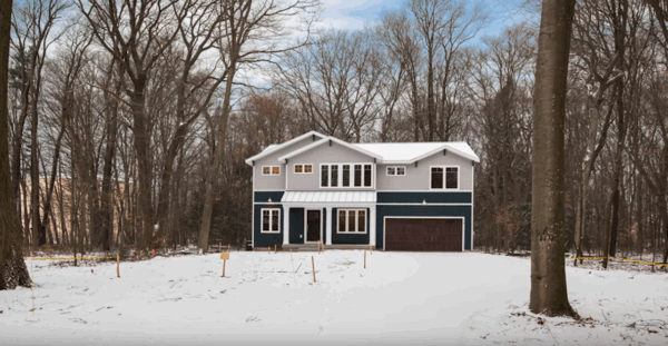 2016slideshow Two-story house with blue and gray siding, a brown garage door, and a covered porch, surrounded by snow and bare trees.