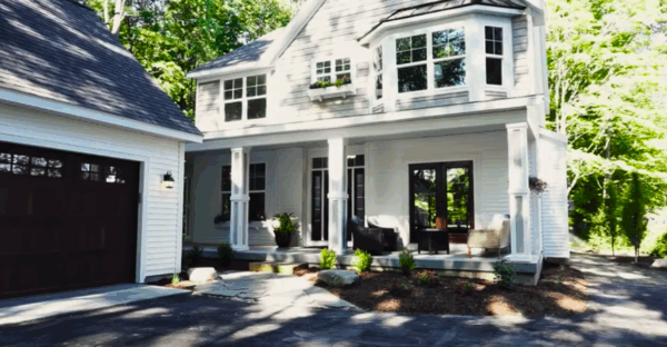 oakhill A two-story white house with a covered porch, plants, and a dark garage door. Surrounded by trees, the house has large windows and a stone pathway leading to the entrance.