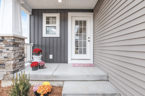palmer Front entry of a house with a glass-paneled door, gray siding, stone accent, and potted red and yellow flowers on concrete steps.