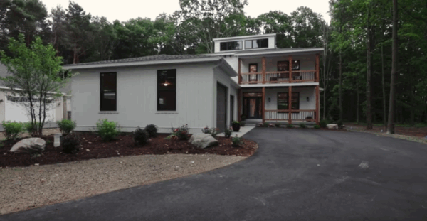 the-sweetbriar Modern white house with a three-story design, large front porch, and surrounding trees. A driveway leads to the garage on the left.