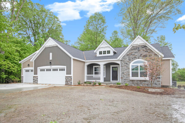 IMG_9099- A single-story house with a mix of stone and siding exterior, three-car garage, and a front porch, set amidst surrounding trees.