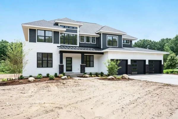 DSC04565 A two-story modern house with a white facade, dark window trim, and a three-car garage. The yard is under landscaping with some bushes and young trees planted in front.