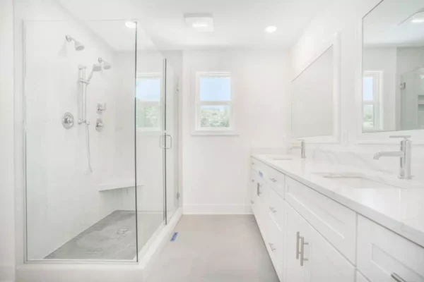 DSC04607 A modern bathroom with a glass-enclosed shower, white cabinets, a double sink vanity, and large mirror. The room has white walls and a minimalist design.