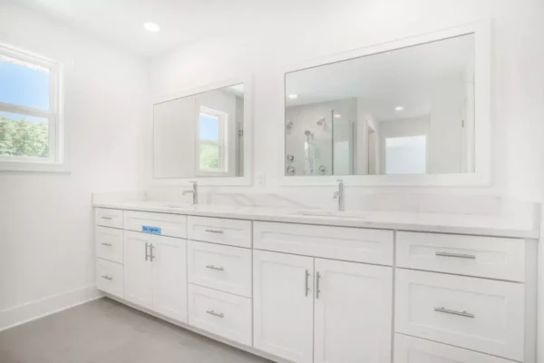 DSC04610 A modern white bathroom features a double sink vanity with ample counter space, large mirrors, and bright natural lighting from a window.