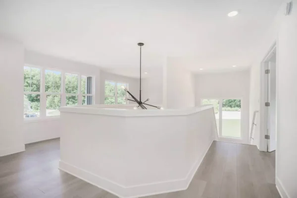 DSC04615 A minimalist upper floor landing with white walls, a black chandelier, large windows on the left, and light wood flooring. Bright natural light fills the space from the windows and staircase area.