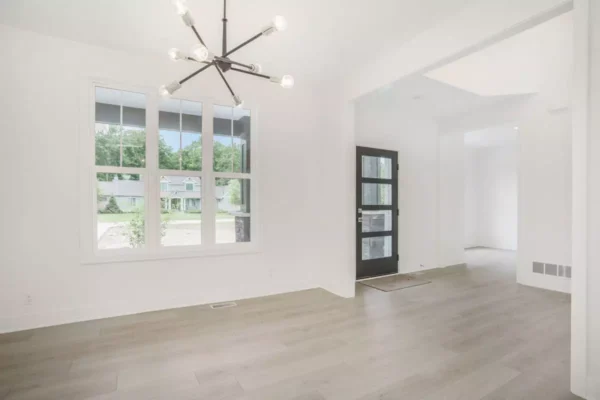 DSC04646 A bright, empty room with light wood flooring, large windows, a modern chandelier, and a glass front door.