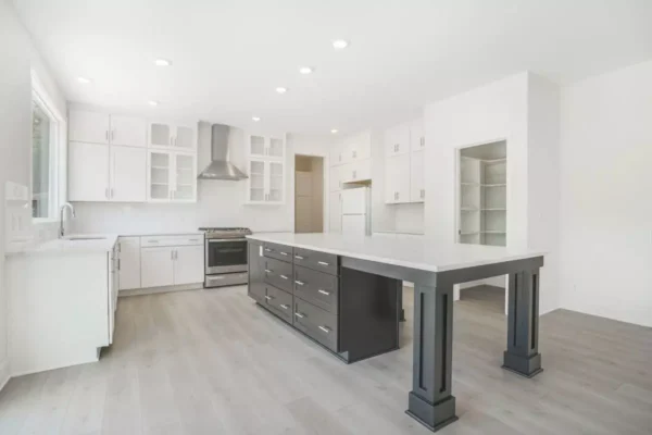 DSC04658 Modern kitchen with white cabinetry, a stainless steel range hood, and a large island with dark drawers. Light wood flooring and ample recessed lighting create a bright, open space.