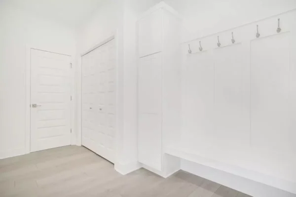DSC04667 Minimalist white room featuring a bench with coat hooks, a tall storage cabinet, and dual-panel doors; floor is light wood.