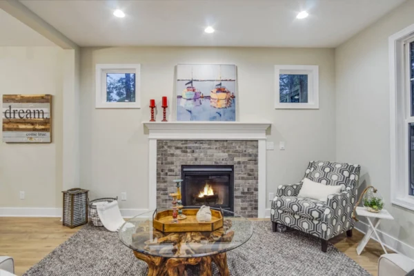 DSC08187Blended Cozy living room with a lit fireplace, patterned armchair, and a glass coffee table on a rug. Artwork above the mantle.