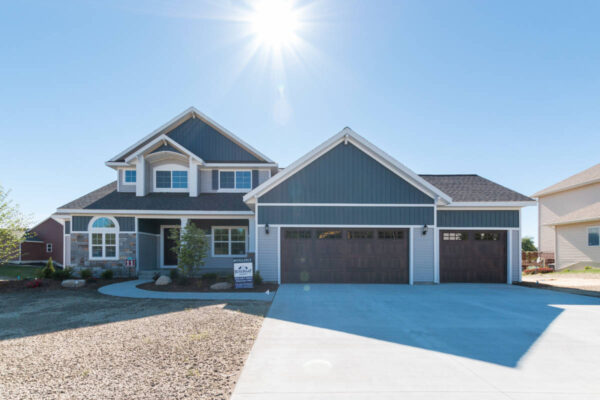 IMG_0247 Two-story blue and gray house with a double garage, driveway, and clear sky with bright sun overhead.