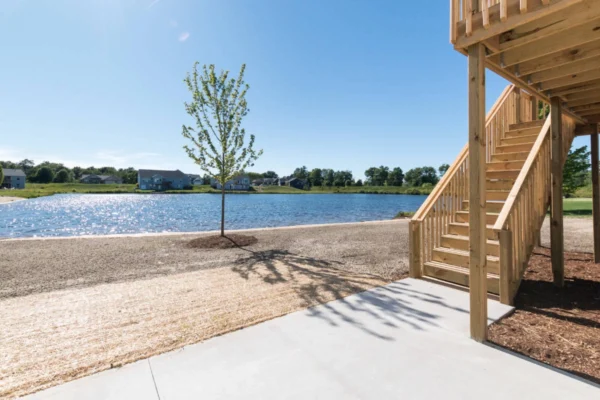 IMG_0260 Wooden deck stairs overlooking a serene lake and tree under a clear blue sky.