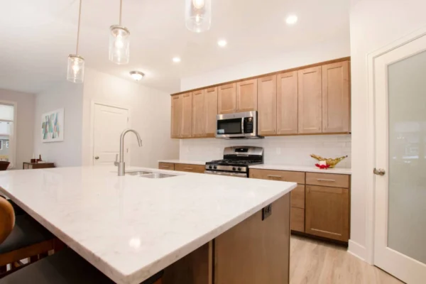 IMG_0273 Modern kitchen with wood cabinets, marble island, stainless steel appliances, and pendant lighting.