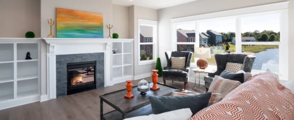 IMG_0286 edit Bright living room; fireplace, art, large windows view, gray chairs, patterned sofa, wooden coffee table with decor.