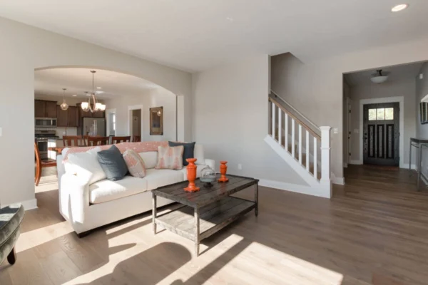 IMG_0290 Bright living room with a white sofa, wooden coffee table, orange vases, and visible staircase leading upstairs.