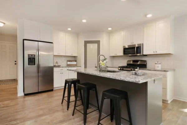 IMG_4696 Modern kitchen with stainless steel appliances, white cabinets, a gray island with three black stools, and a granite countertop.