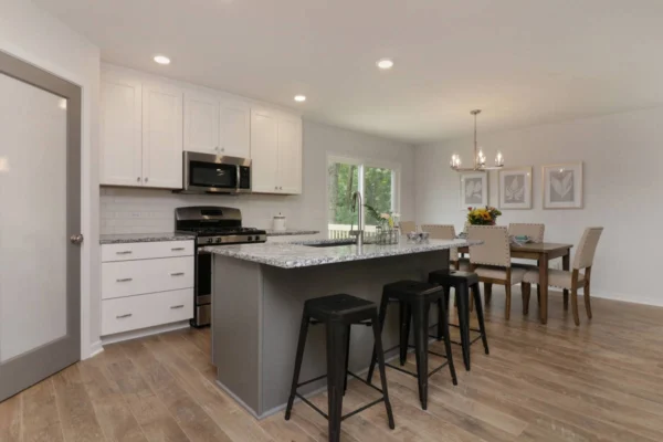 IMG_4699 Modern kitchen with a central island featuring three bar stools, stainless steel appliances, white cabinets, and a dining area with a table, chairs, and a chandelier.