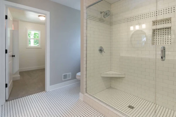 IMG_4879 Modern bathroom with a glass shower, white subway tiles, and black-and-white patterned floor tiles.
