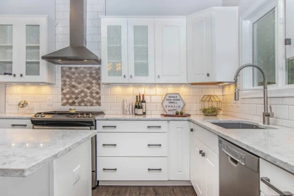 IMG_5991 Modern kitchen with white cabinetry, stainless steel appliances, marble countertops, and a tiled backsplash. A window above the sink and recessed lighting brighten the space.