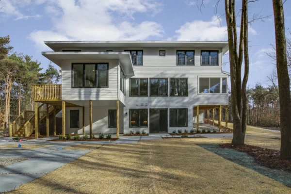 IMG_6399Blended Modern three-story house with large windows, surrounded by trees, under a partly cloudy sky.