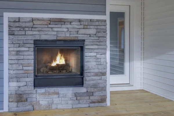 IMG_6441Blended A stone fireplace with a lit fire on a wooden patio next to a glass door.