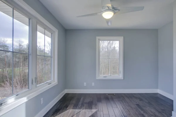 IMG_6471Blended Bright room with gray walls, large windows, dark wood floors, and a ceiling fan. Trees visible outside.
