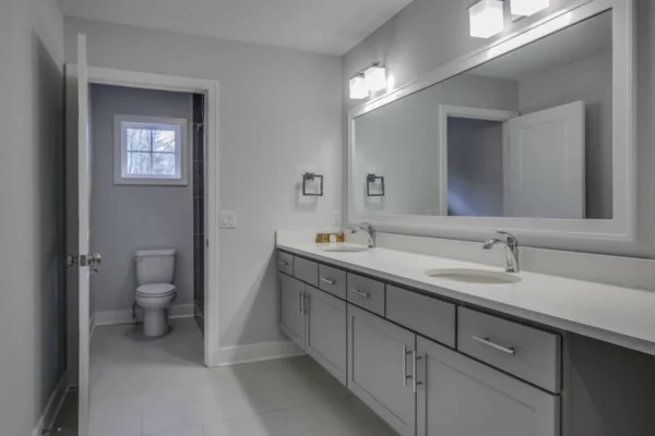 IMG_6492Blended Modern bathroom with double sink vanity, large mirror, and toilet in a separate room. Walls and cabinets are grey.