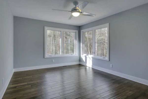 IMG_6498Blended An empty room with gray walls, dark wooden floors, large windows, and a ceiling fan.