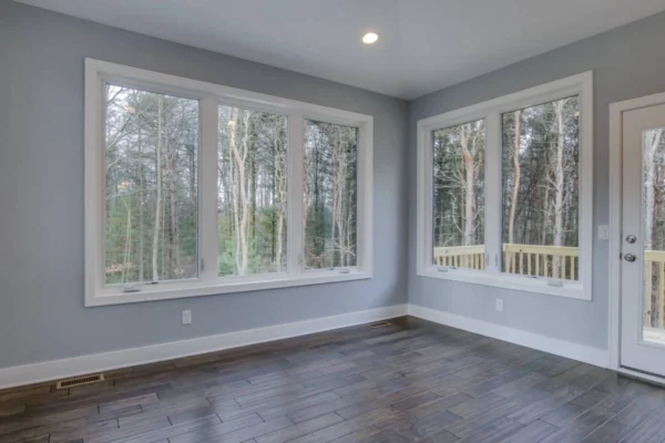 IMG_6540Blended Room with large windows overlooking a forest, gray walls, wooden floor, and a door leading to a small deck.