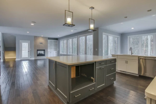 IMG_6555Blended Spacious modern kitchen with island, pendant lights, hardwood floors, and large windows overlooking a wooded area.