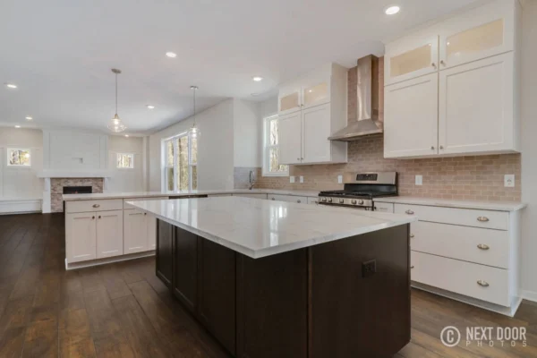 IMG_7610_blended Modern kitchen with a large island, white cabinets, stainless steel appliances, and wood flooring.