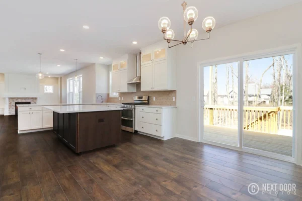 IMG_7646_blended Modern kitchen with dark wood flooring, white cabinets, island, chandelier, and sliding glass doors to a wooden deck.