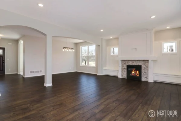 IMG_7667_blended-a Spacious living room with dark wood floors, white walls, fireplace, and a modern light fixture.