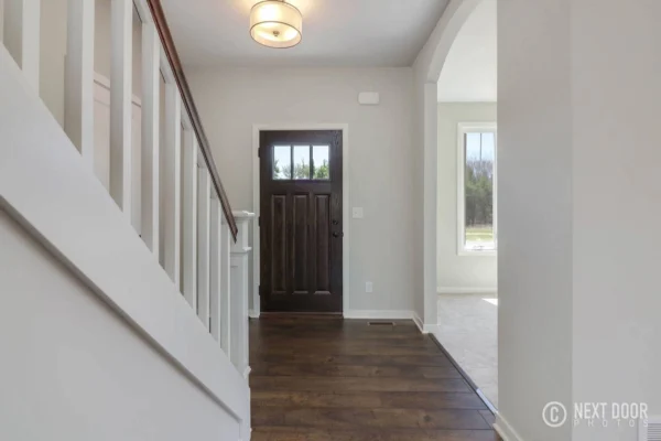 IMG_7676_blended Modern entryway with dark wooden door, staircase, and hardwood floors. Bright natural light from side windows.