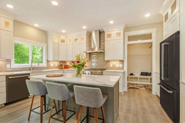 IMG_9936 Modern kitchen with a central island, three stools, flowers, white cabinets, and stainless steel appliances.
