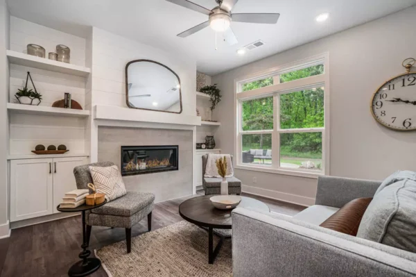 DSC00091 Step into a stylish living room featuring a gray sofa, round coffee table, and fireplace, with a large window overlooking lush greenery. Discover the beauty of modern design and explore current promotions to transform your space today.