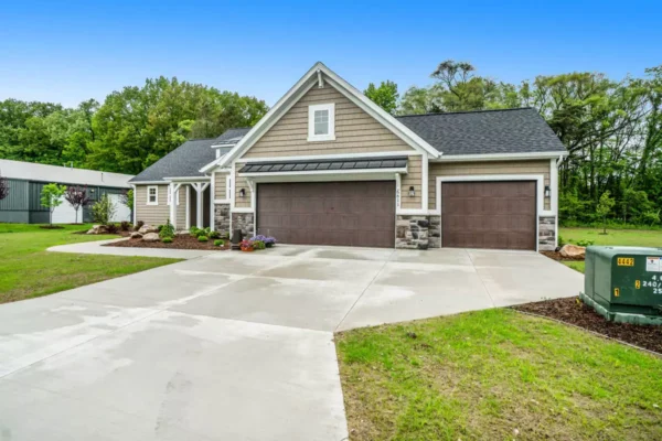 DSC00098 Modern suburban house with three garage doors, stone and siding exterior, and a large concrete driveway.