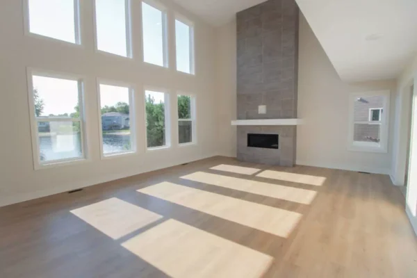 IMG_4599 Bright, empty living room with large windows, wood flooring, and a tall tile fireplace.