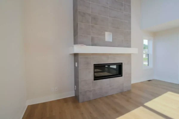 IMG_4601 Modern fireplace with gray tile surround, white mantel, and light wood floor in a bright, empty room.