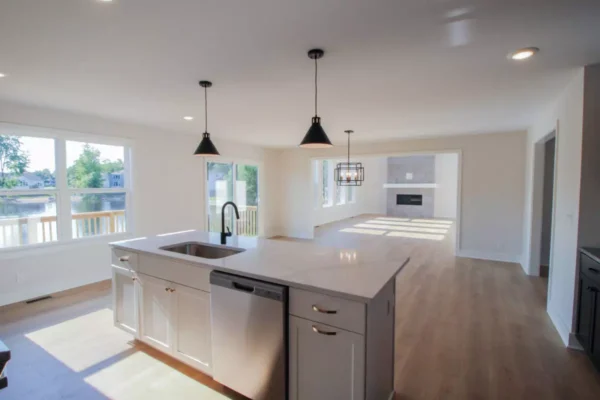 IMG_4624 Bright modern kitchen with island and open living area, wood floors, large windows, and pendant lights.